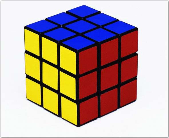 
Una imagen del popular cubo rubik. El cubo está completo y muestra tres de sus caras. La roja, la azul y la amarilla. En cada cara hay nueve cuadraditos iguales entre sí, pero distintos en color a los de las otras caras. 
